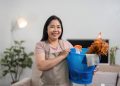 Smiling cleaner holding a bucket of cleaning supplies in a bright home — starting a cleaning business with no money