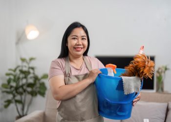 Smiling cleaner holding a bucket of cleaning supplies in a bright home — starting a cleaning business with no money