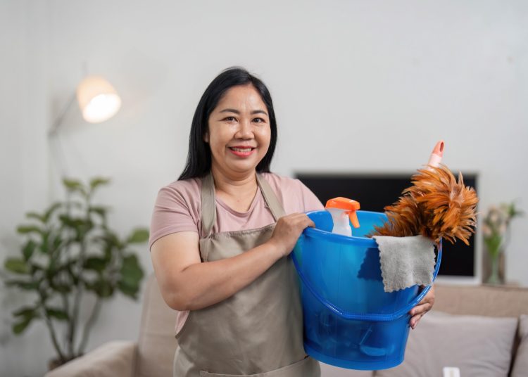 Smiling cleaner holding a bucket of cleaning supplies in a bright home — starting a cleaning business with no money