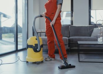 Professional cleaner in red coveralls vacuuming a living room